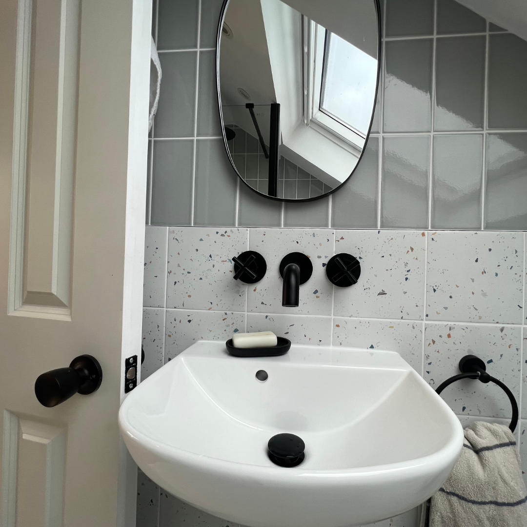 Modern loft bathroom with terrazzo tiles and sleek black fixtures in Catford, South London.