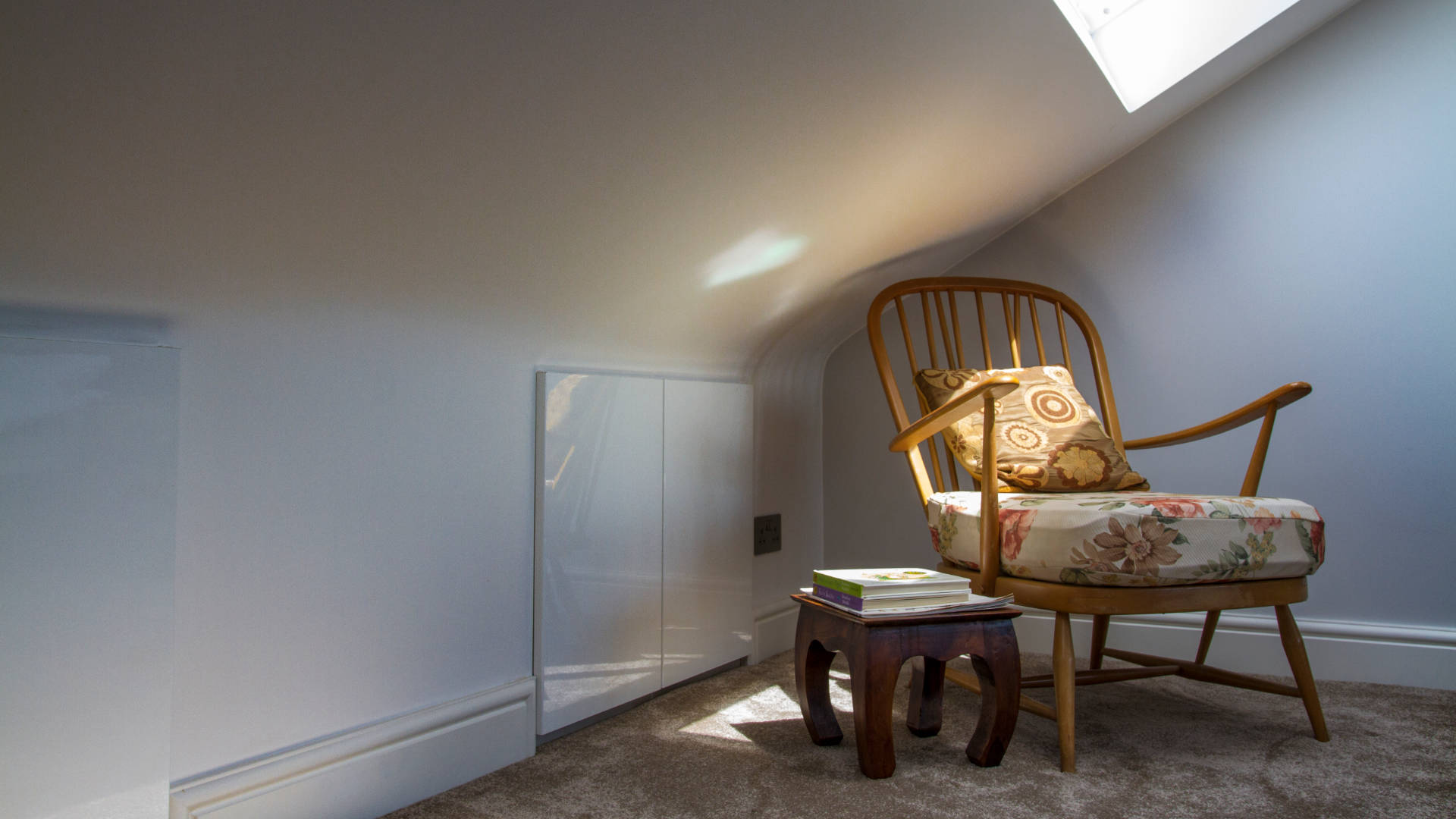 A chair sits in a shaft of sunlight from a Velux window in a bright, spacious loft bedroom in Catford.