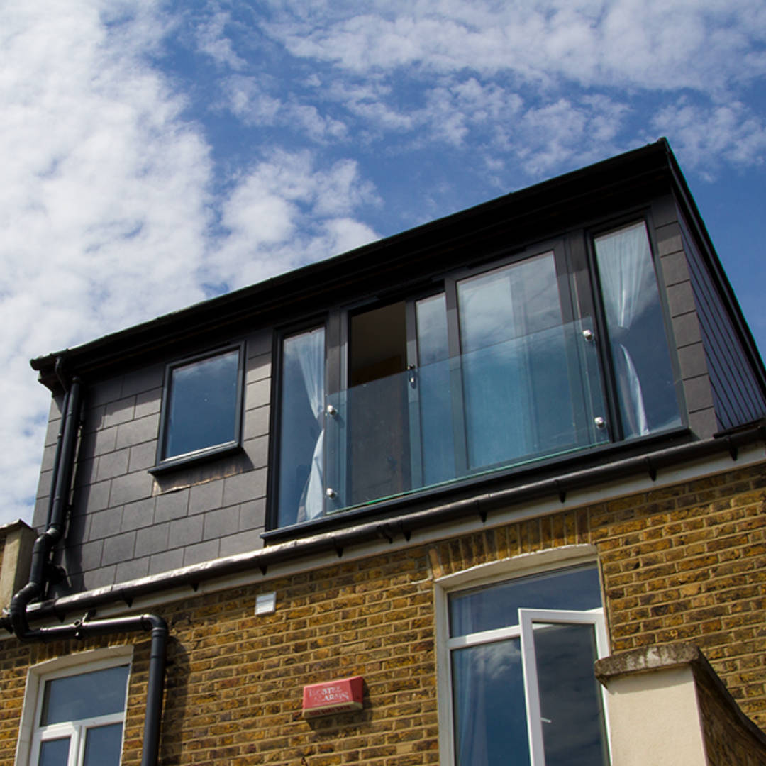 braidwood-road-detail-exterior A modern loft conversion clad in sleek grey slate stands against a blue sky in South London.