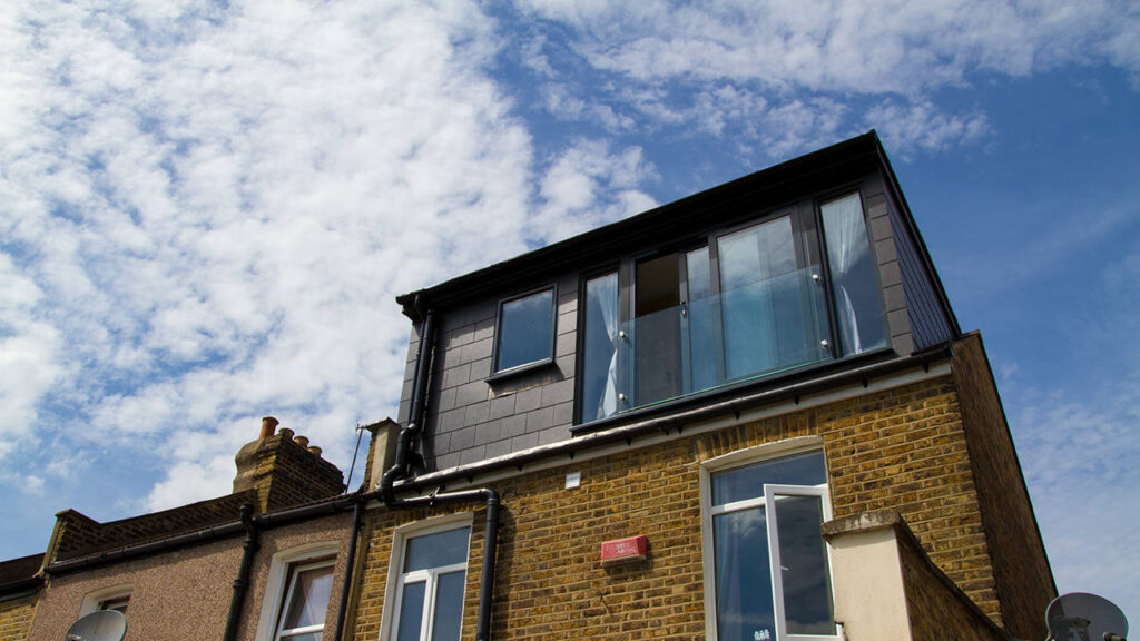 The exterior of modern loft conversion clad in sleek grey slate stands against a blue sky in Catford, South London.