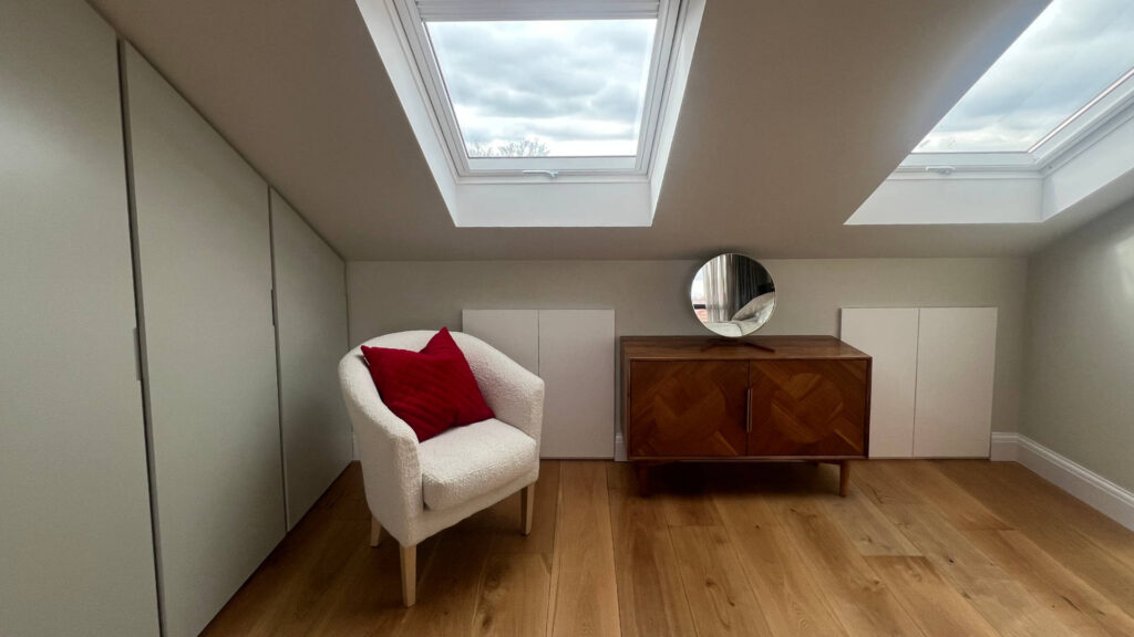 Large Velux windows spill light into this spacious loft bedroom in Herne Hill, South London. To the side, sleek built-in storage makes the most of the available wall-space.